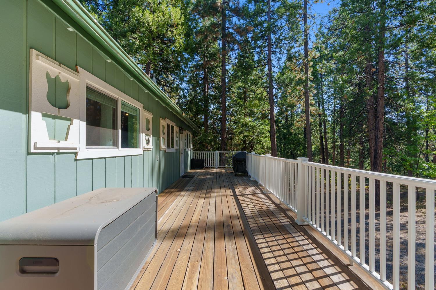 Wooden deck beside a green-sided home, bordered by white railings and tall trees.