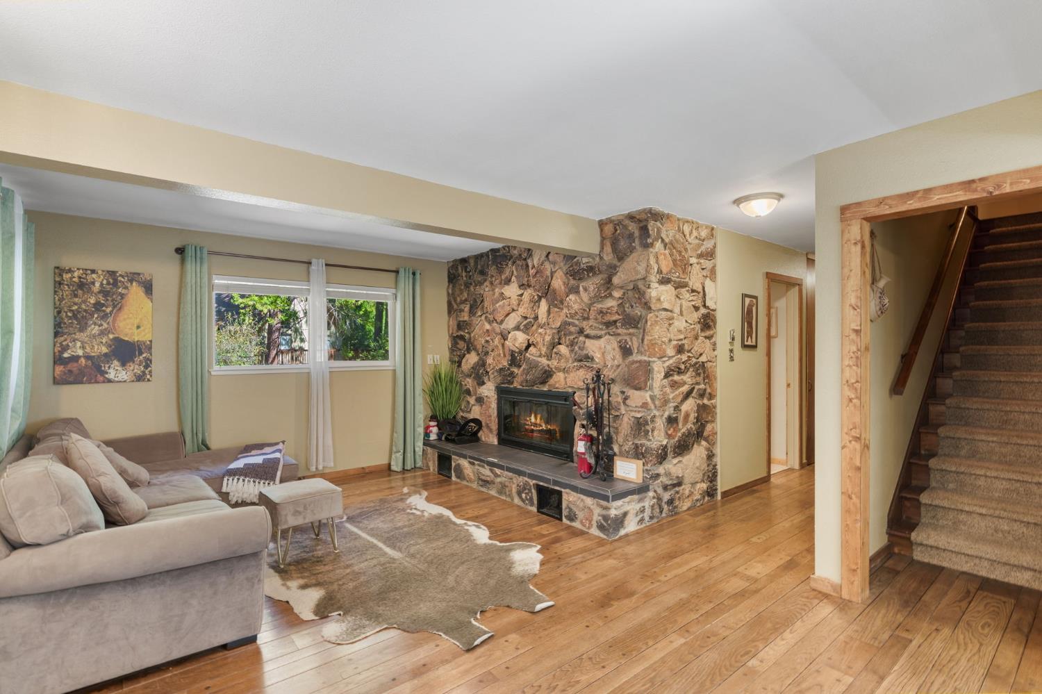 Living room with a floor-to-ceiling stone fireplace, hardwood floors, and carpeted stairs.