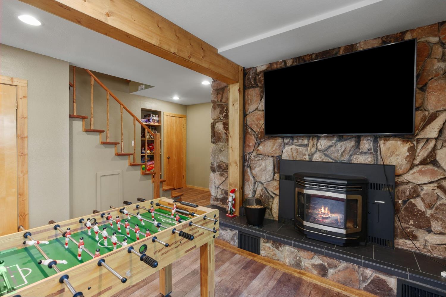 Recreation room with a foosball table, stone fireplace, and large wall-mounted television.