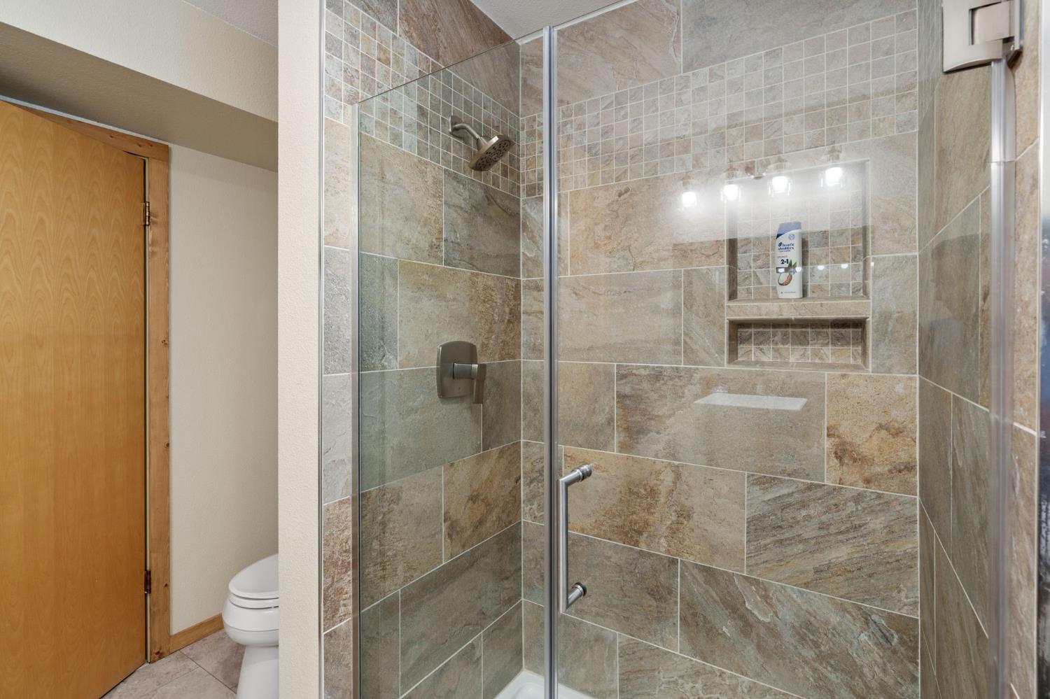 Tiled walk-in shower with glass enclosure, built-in niche, and ceiling-mounted showerhead.