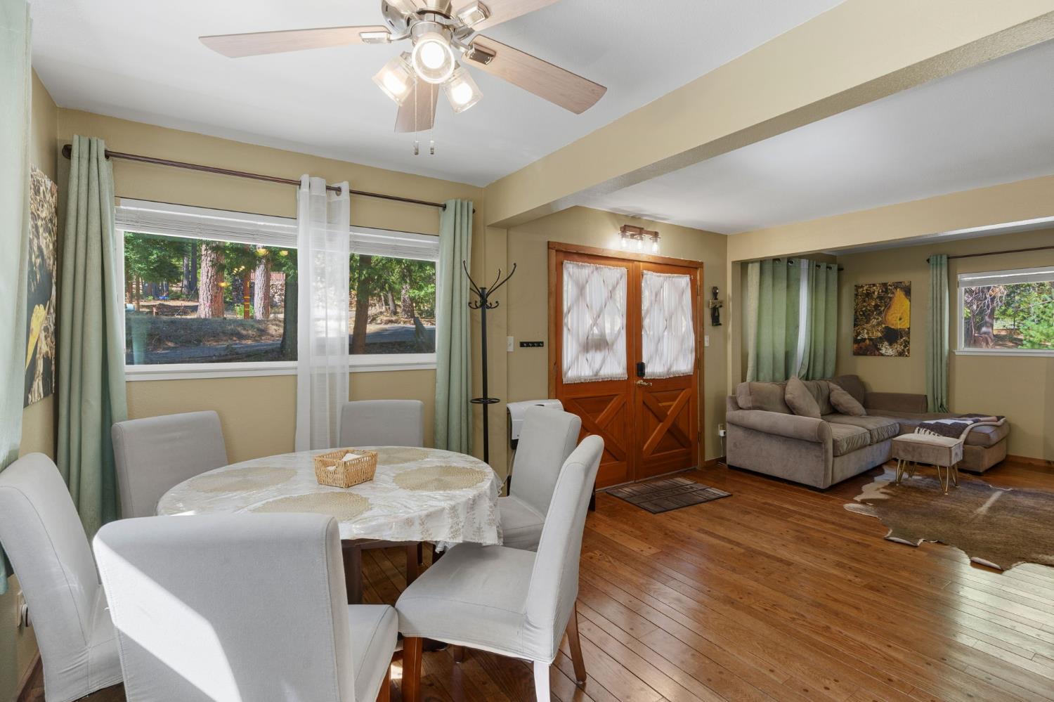 Dining and living area with white dining chairs, wood floors, wood double doors, and a sectional sofa.