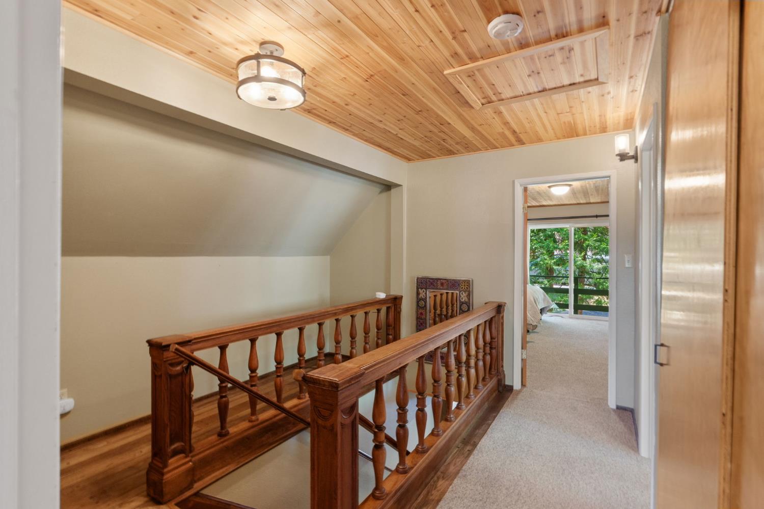 Upstairs landing with dark wood stair railings and a wood plank ceiling.