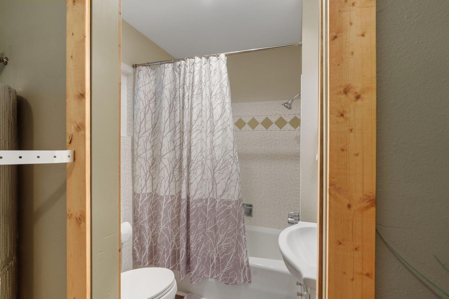 Bathroom with a branch-patterned shower curtain, bathtub, and white sink.