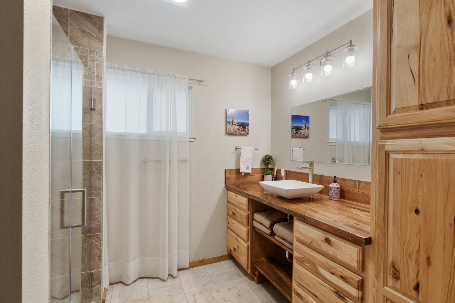 Bathroom with a glass shower and long rustic wood vanity with vessel sink.