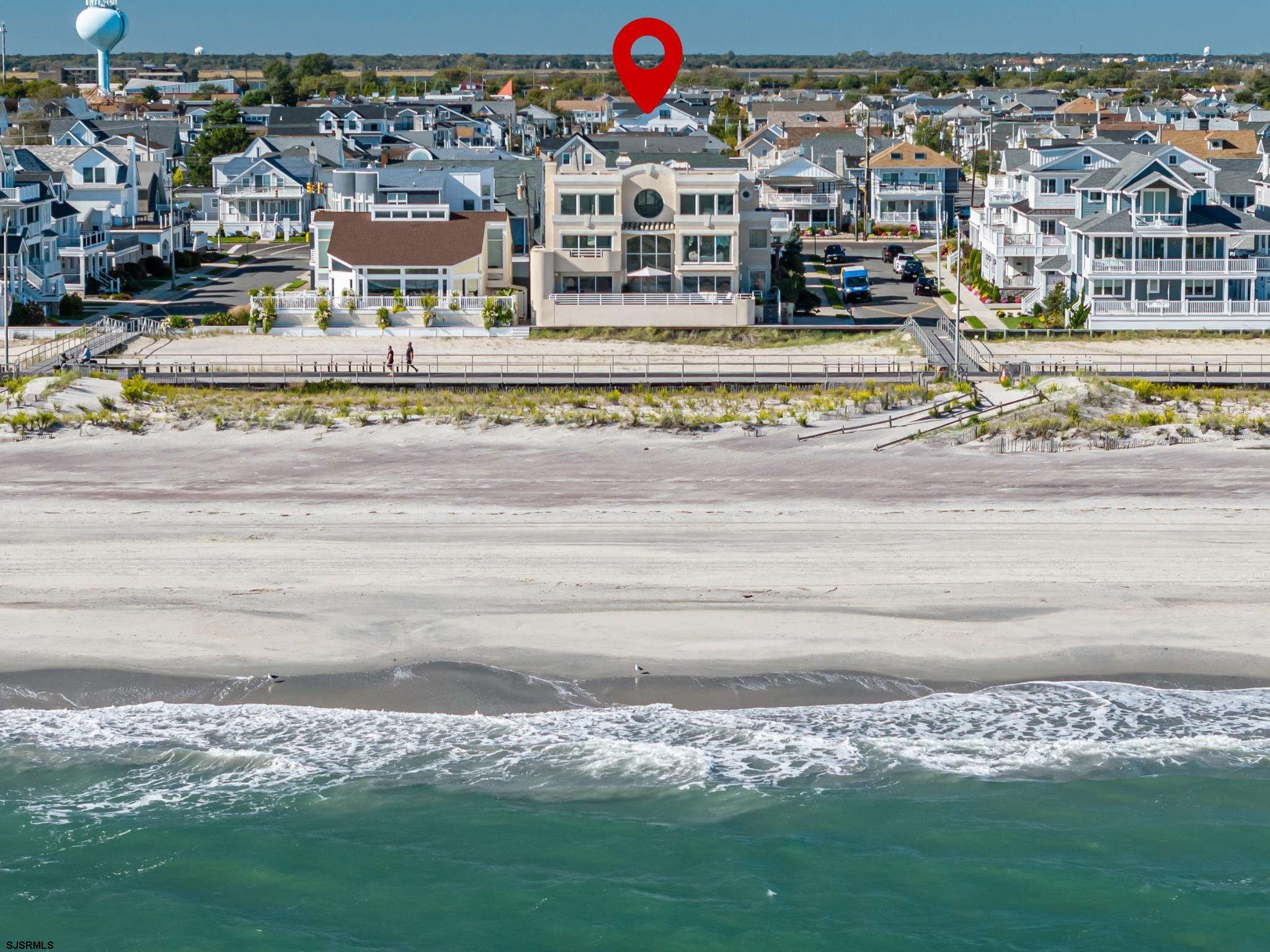 Aerial view of beachfront homes, a sandy beach, and ocean waves, with a red location pin.