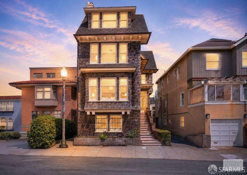 Tall shingle-clad San Francisco home with projecting bay windows and a steep front staircase at dusk.