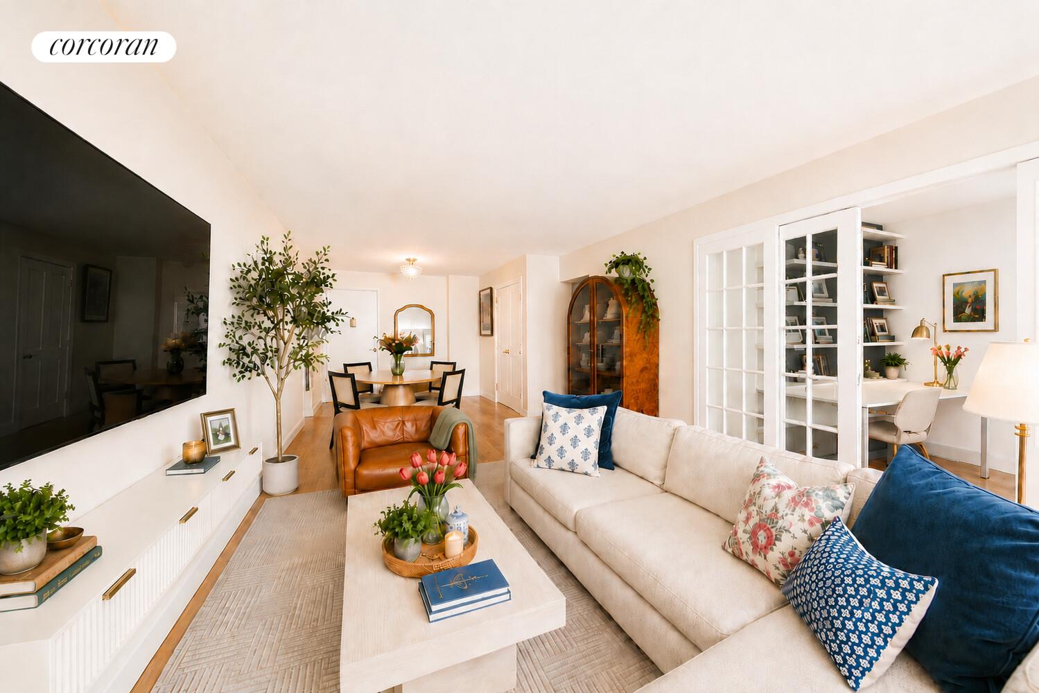 Furnished living room with a cream sectional, blue accent pillows, dining area, and glass-door home office.