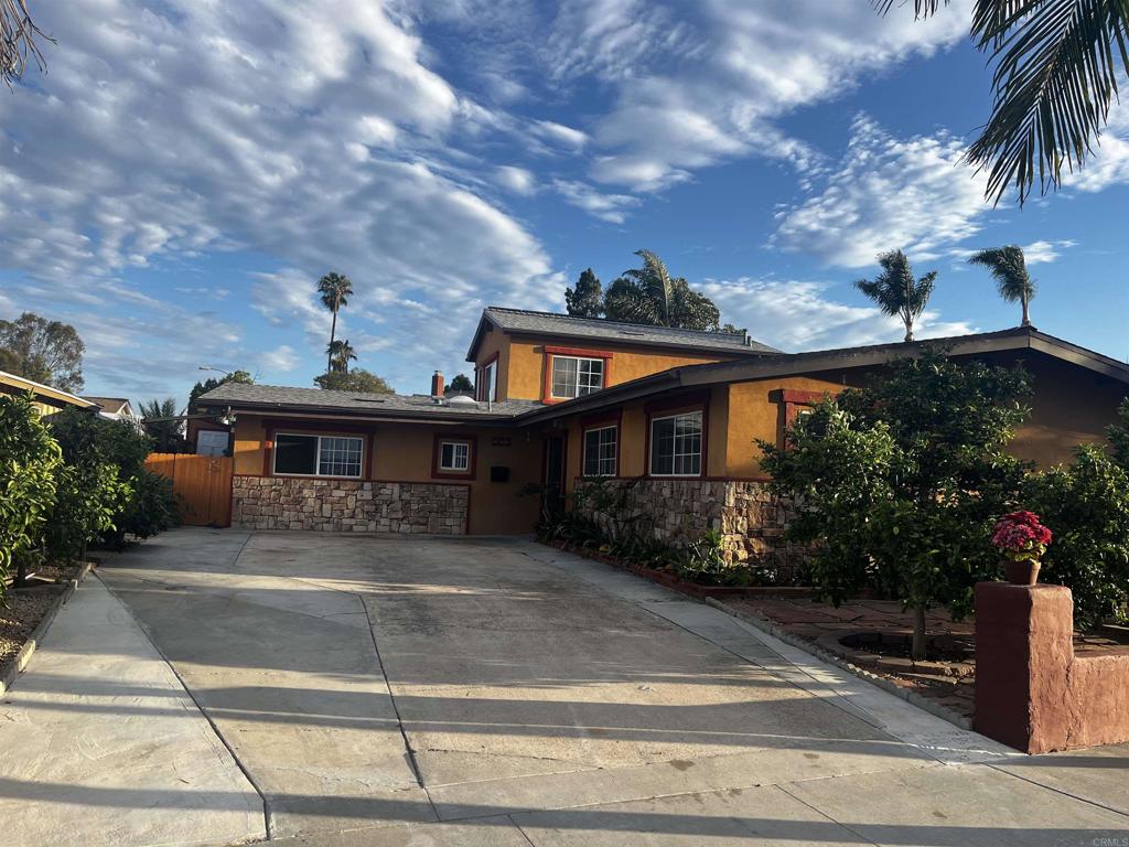 Orange stucco home with stone veneer, wide driveway, and tropical landscaping.