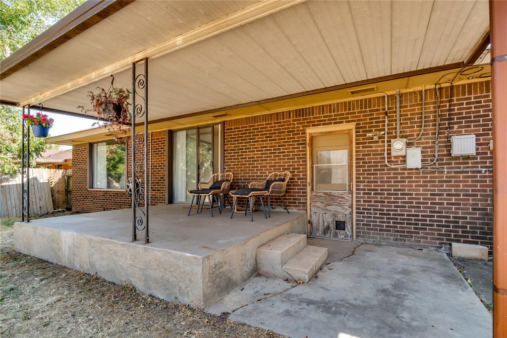 Brick home’s covered back patio with metal supports, concrete steps, and chairs.