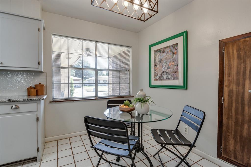 Kitchen dining nook with a round glass table and black metal chairs beside a large window.