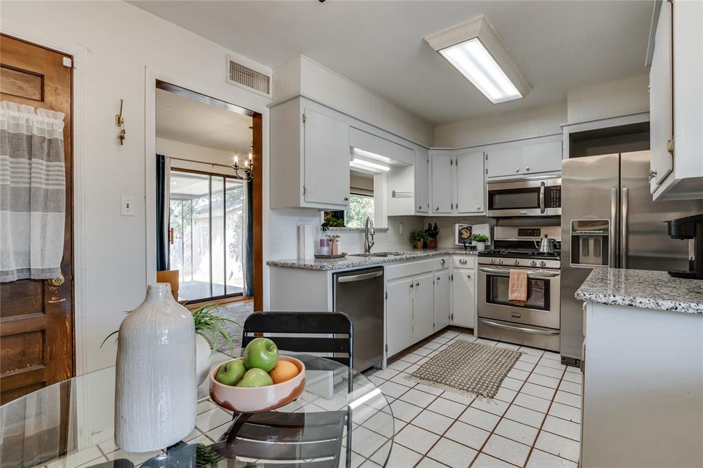 Kitchen with white cabinets, stainless steel appliances, and a glass dining table by a sliding door.