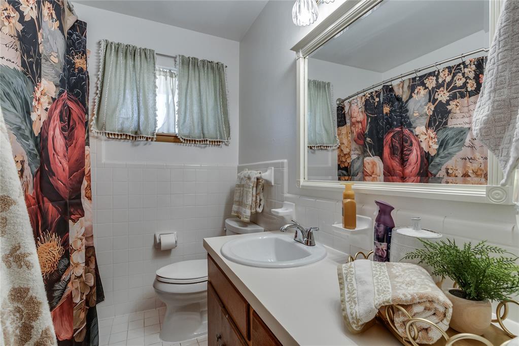 Bathroom with a wood vanity, white sink, and bold floral shower curtain reflected in the mirror.