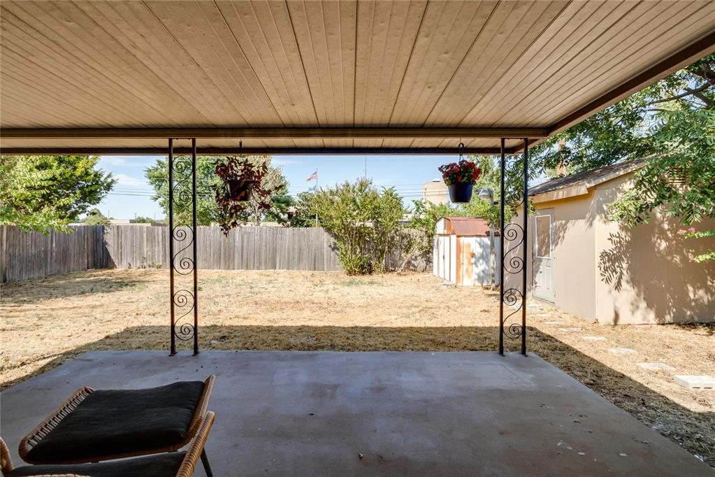 Covered concrete patio overlooking a fenced backyard with a small storage shed.