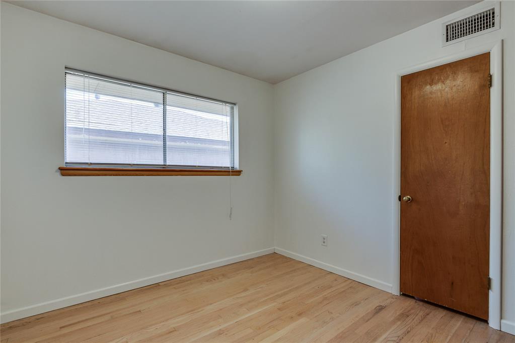 Empty room with hardwood floors, a wide window with blinds, and a wooden door.