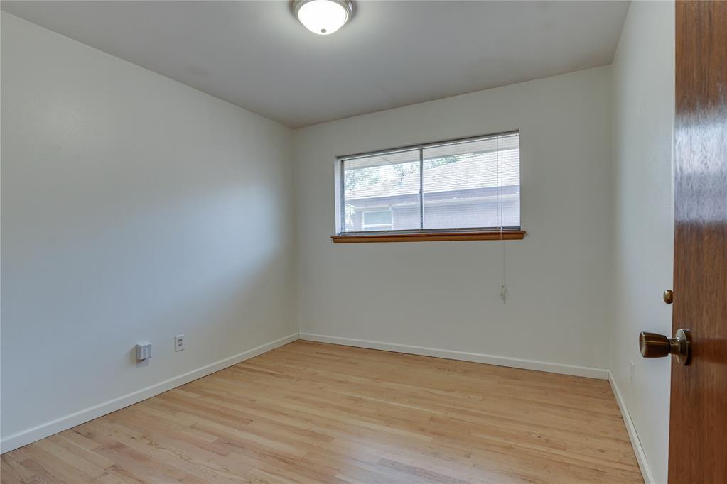 Empty room with light wood floors, a wide window with blinds, and a ceiling light.