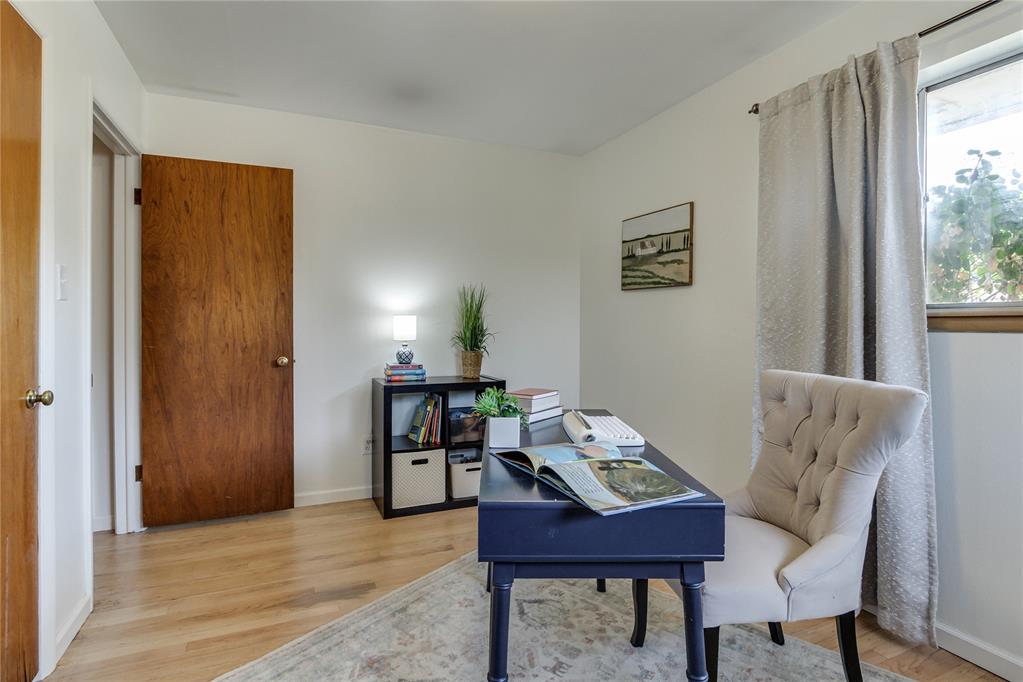 Furnished home office with a dark blue desk and white tufted chair beside a curtained window.