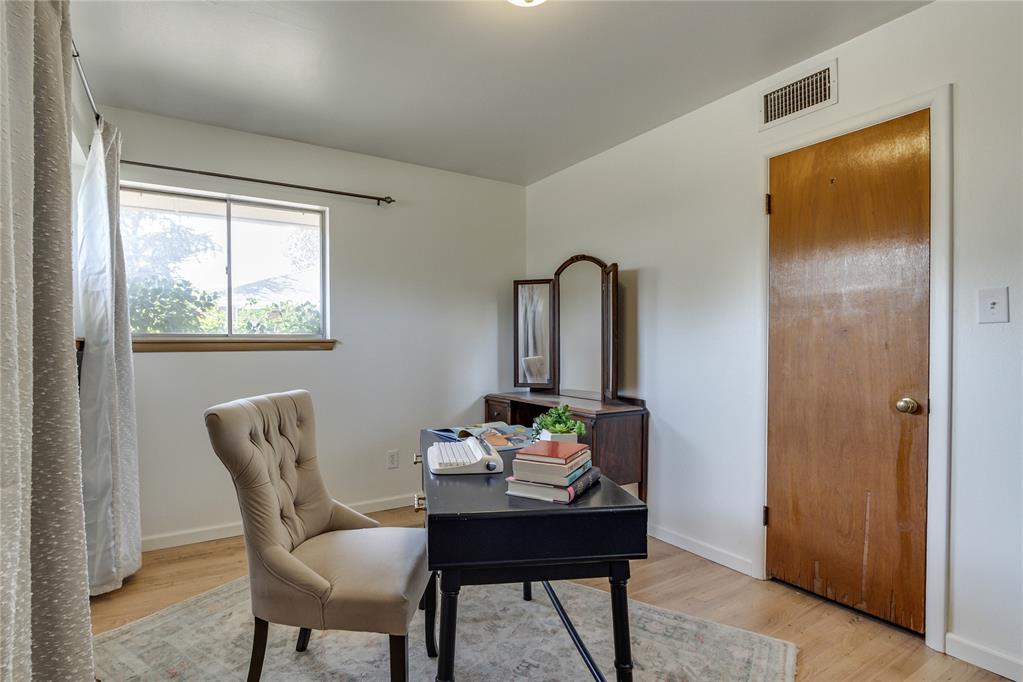 Home office with a black desk, tufted chair, wooden dresser, and window.