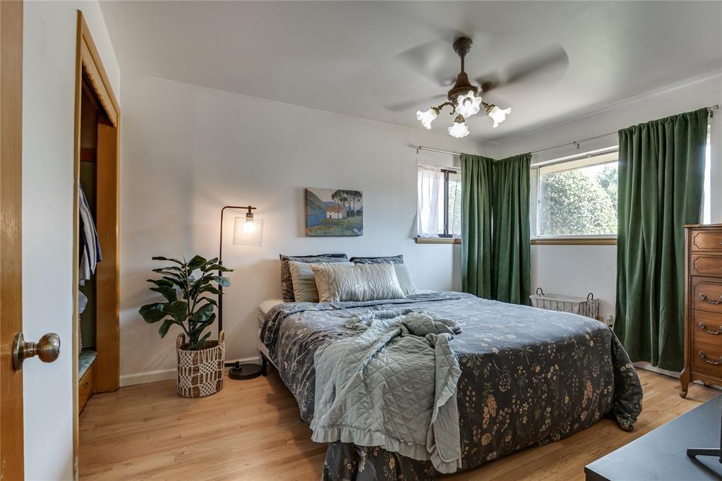 Bedroom with gray patterned bedding, green curtains, and hardwood floors.