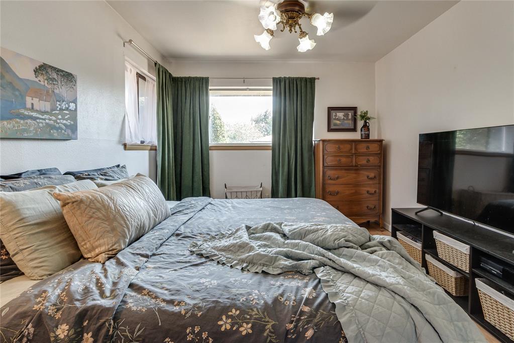 Bedroom with a large patterned bed, green curtains, wooden dresser, and television.