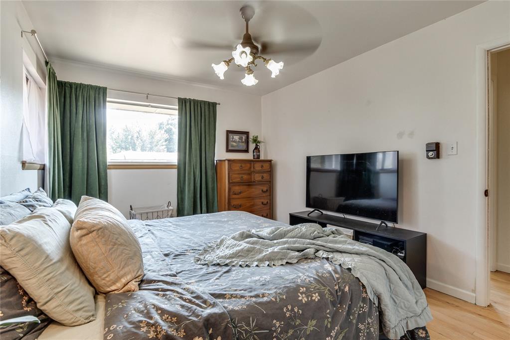 Bedroom with a large floral-covered bed, green curtains, wooden dresser, and television.