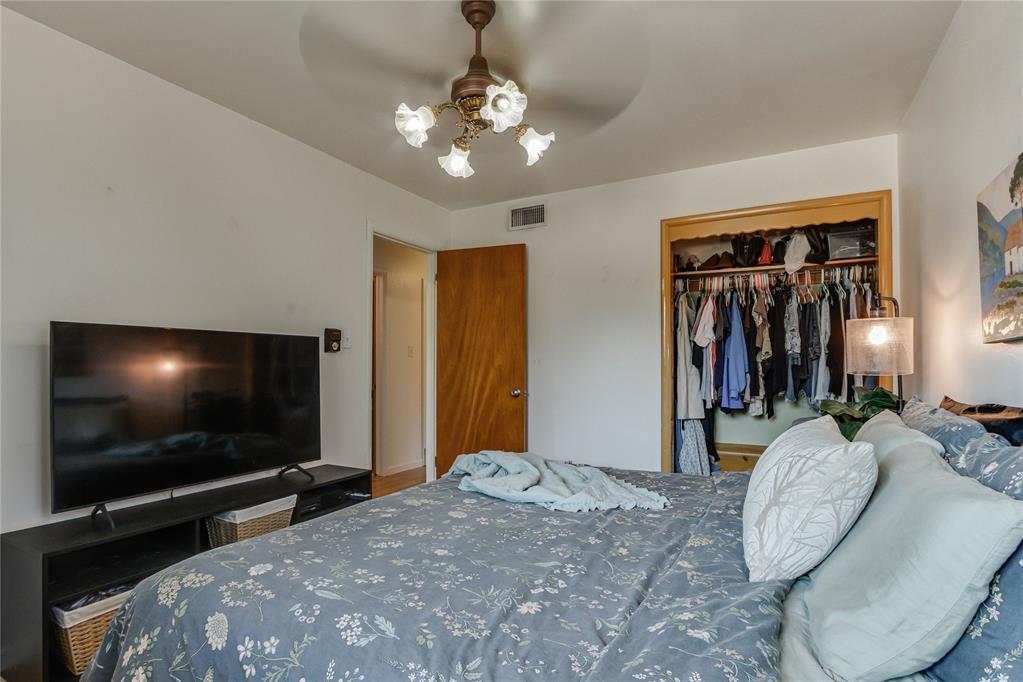 Bedroom with blue floral bedding, a television, and an open closet filled with clothes.