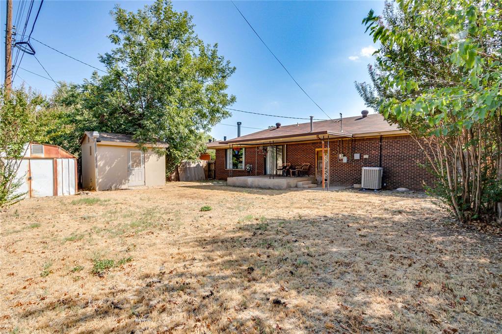 Rear view of a brick home with a covered patio, dry lawn, and two sheds.