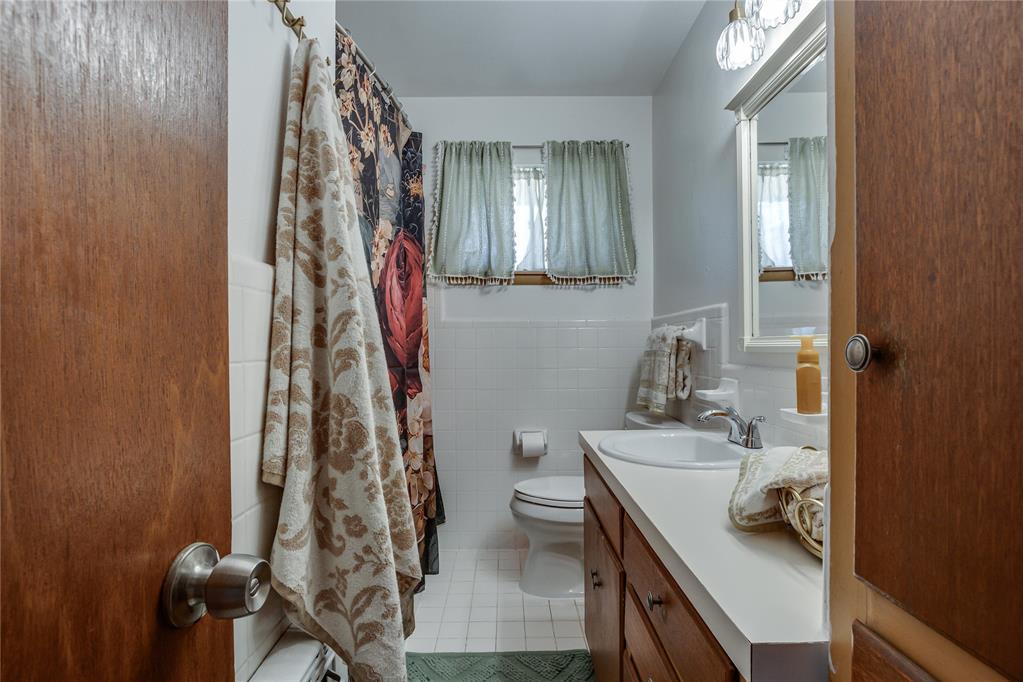 Bathroom with a wood vanity, white tile, and floral shower curtain.