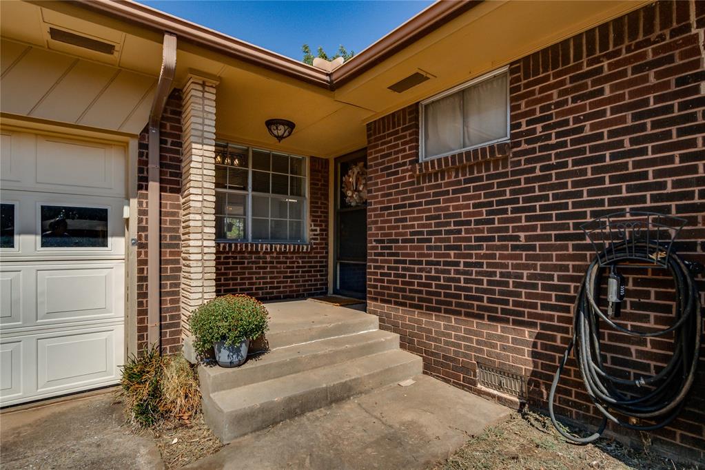Red brick home entrance with concrete steps, a covered porch, and a white garage door.