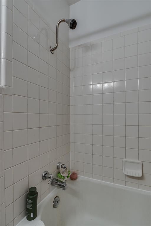 Tiled bathtub and shower with a curved shower arm and built-in soap dish.
