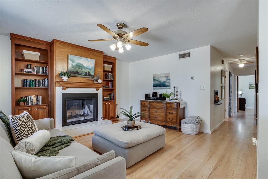 Living room with a built-in fireplace and bookshelves, wood flooring, and a large upholstered ottoman.