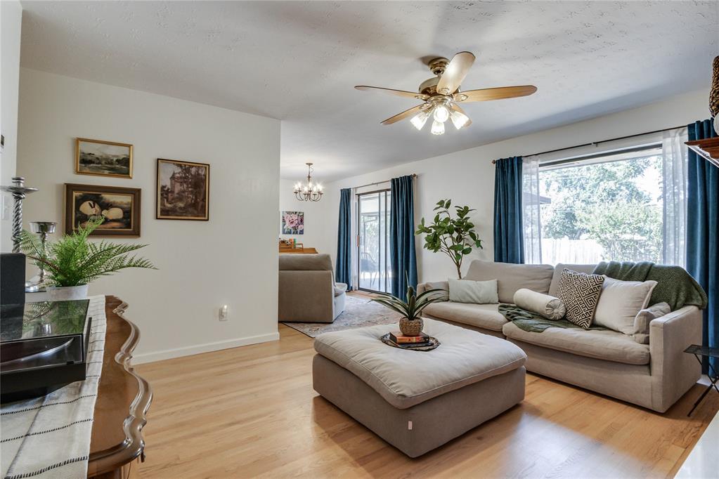 Living room with a beige sectional and ottoman, light wood floors, and large curtained windows.
