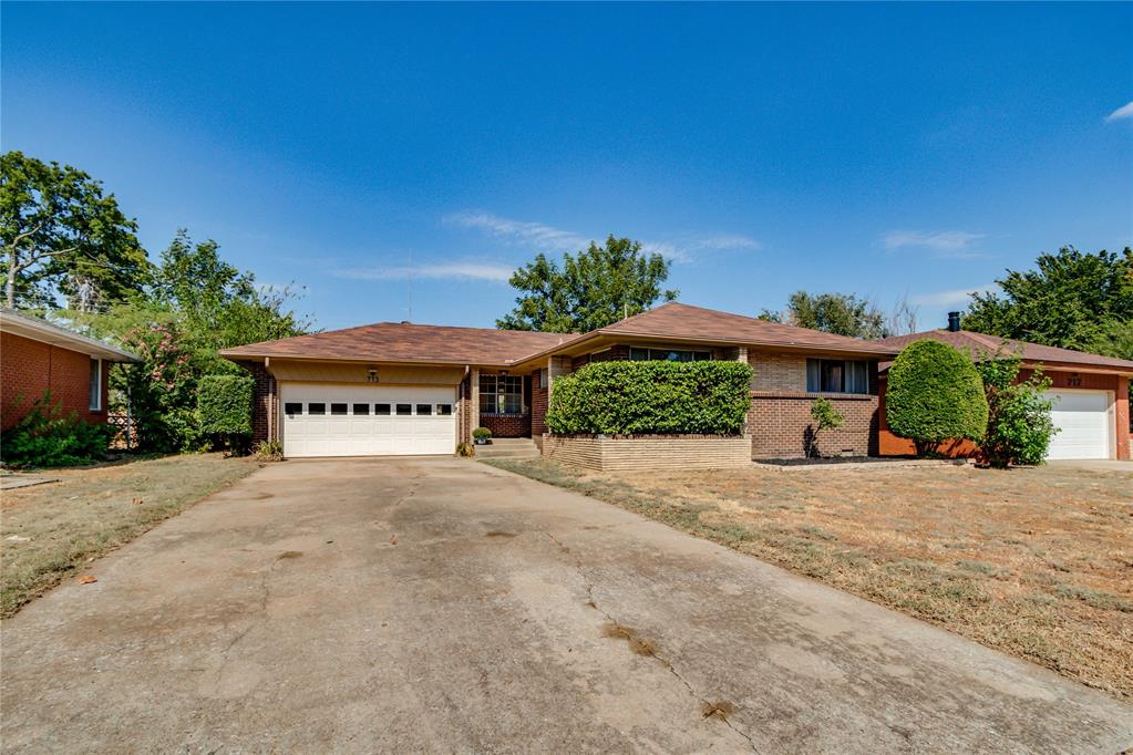 Single-story brick ranch home with a white double garage, wide driveway, and trimmed front shrubs.