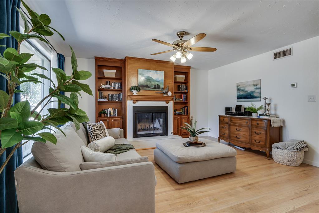 Living room with a wood fireplace and built-in bookshelves, sectional sofa, and hardwood floors.