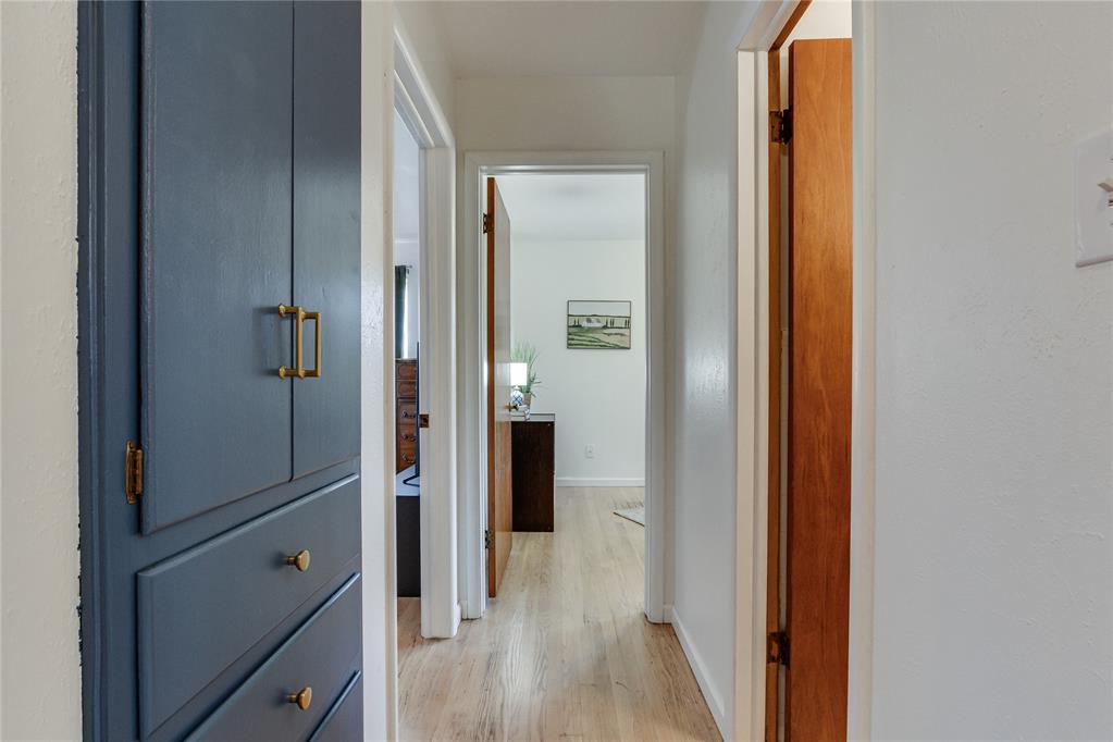 Hallway with dark blue built-in cabinets, brass hardware, and light wood flooring.