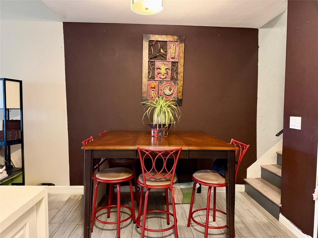 Dining area with a tall wooden table, red stools, and stairs beside a dark accent wall.