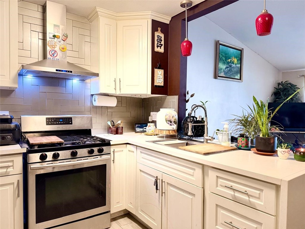 Kitchen with white cabinets, stainless steel range, gray tile backsplash, and red pendant lights.