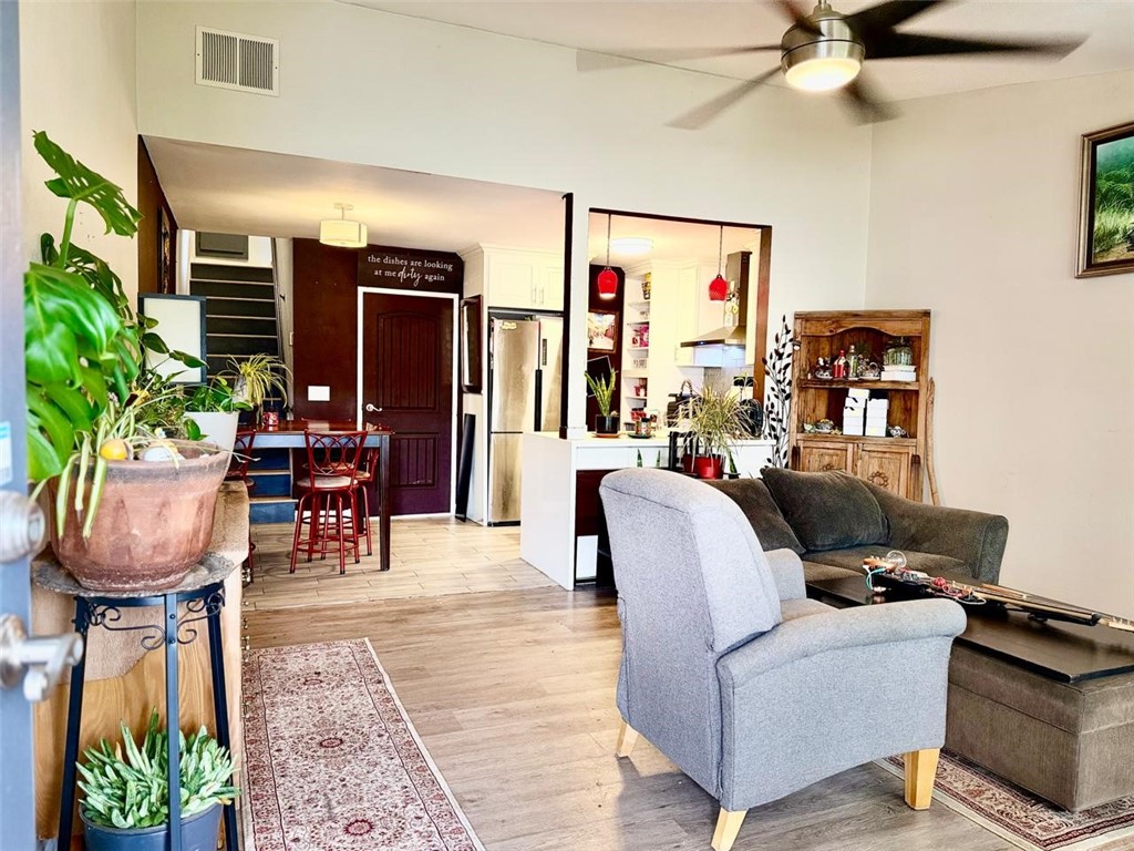 Open-plan living room with gray seating, potted plants, and a kitchen beyond.