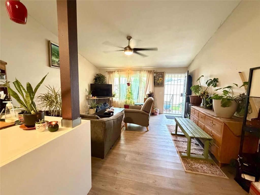 Furnished living room with wood flooring, leafy plants, and a bright glass door.