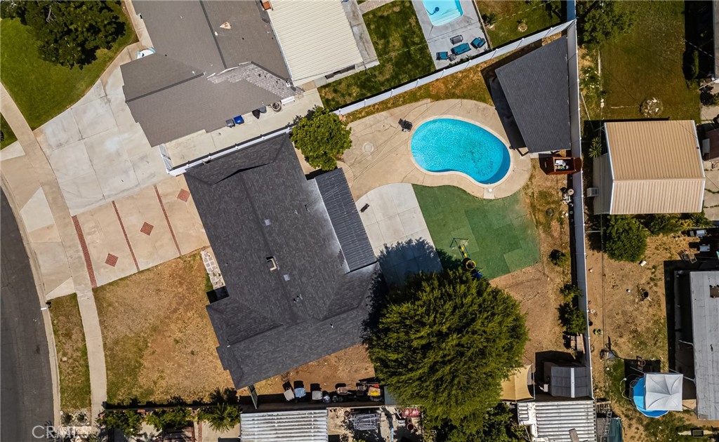 Aerial view of a home with a dark roof, paved driveway, and bright blue backyard pool.