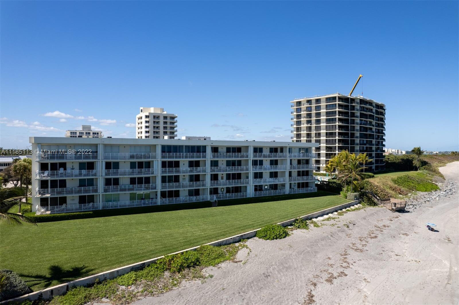Beachfront condominium buildings beside a sandy shoreline and landscaped lawn.