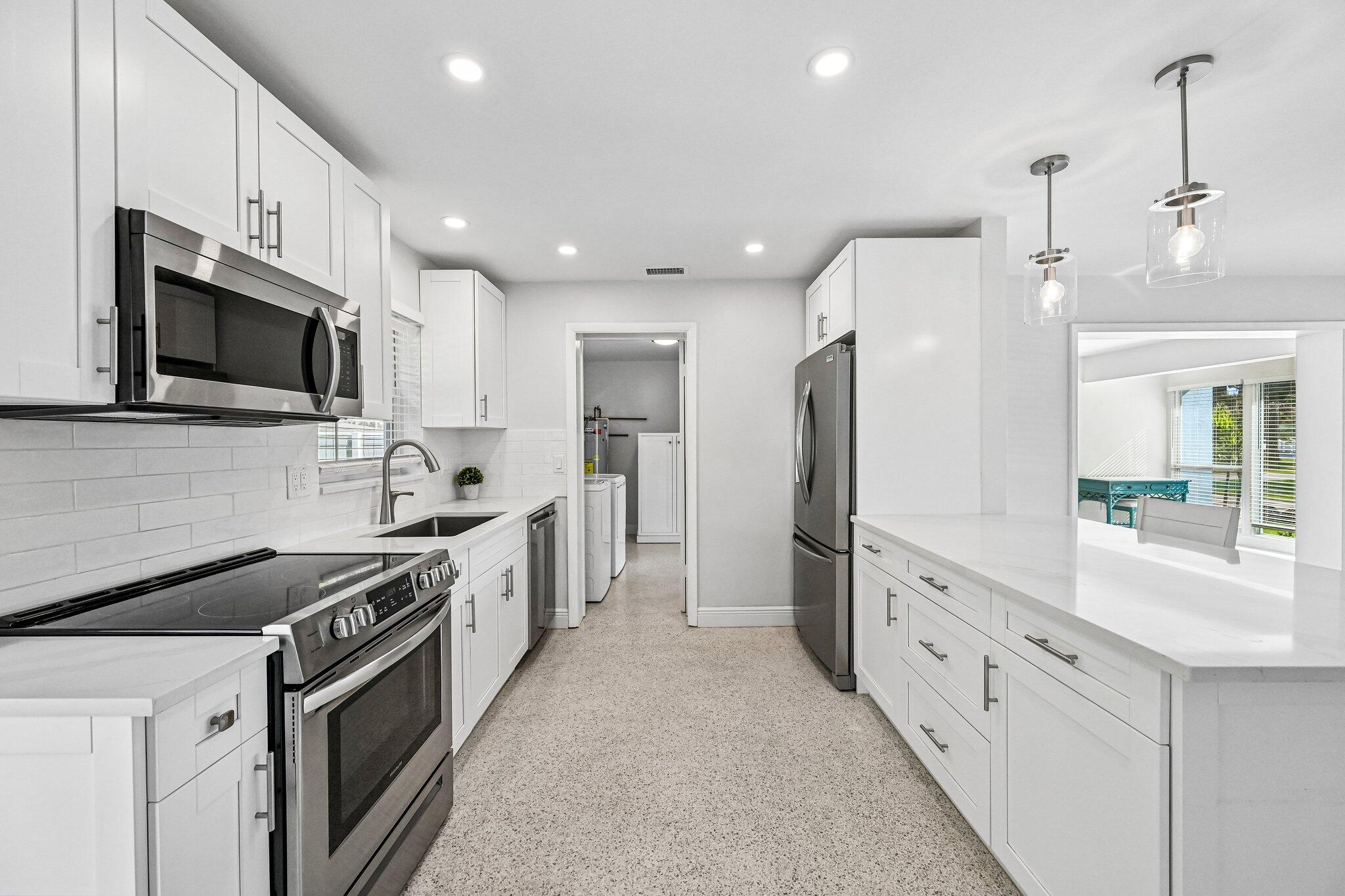 Bright white kitchen with stainless steel appliances, quartz counters, and a pass-through to a sunny dining area.