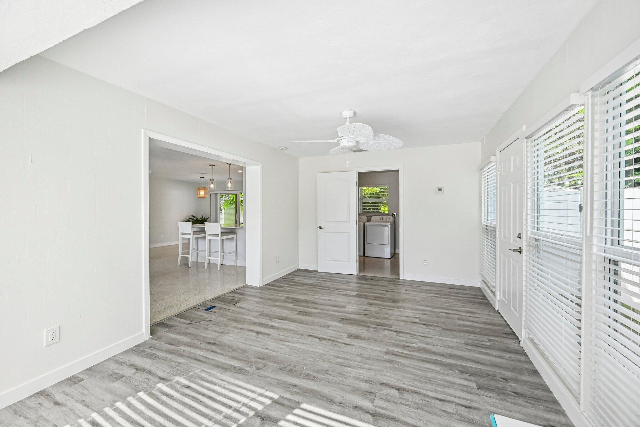 Bright room with gray plank flooring, white blinds, and a view into the dining area and laundry room.