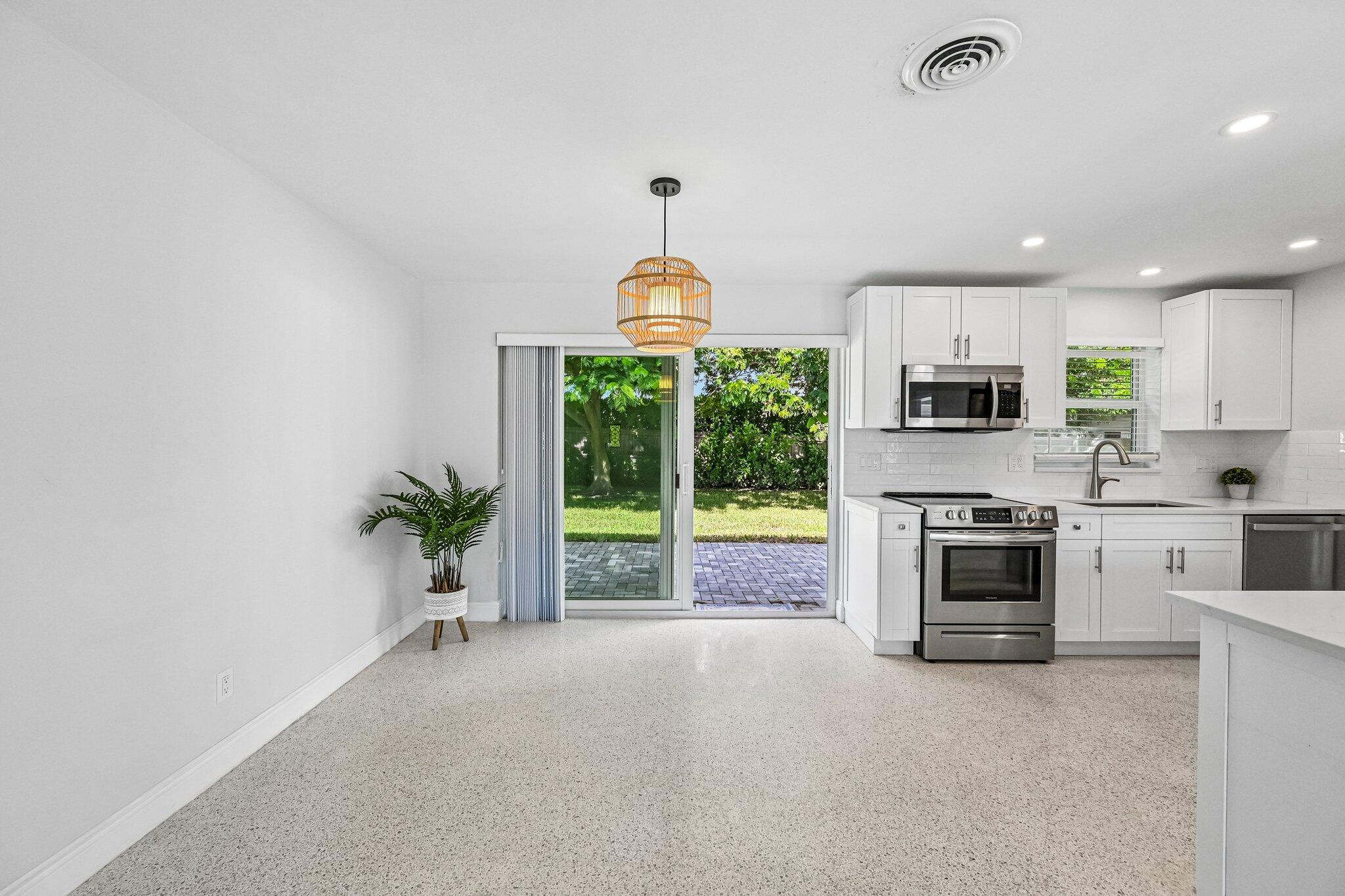 Bright white kitchen with stainless steel appliances and sliding doors opening to a paved patio.