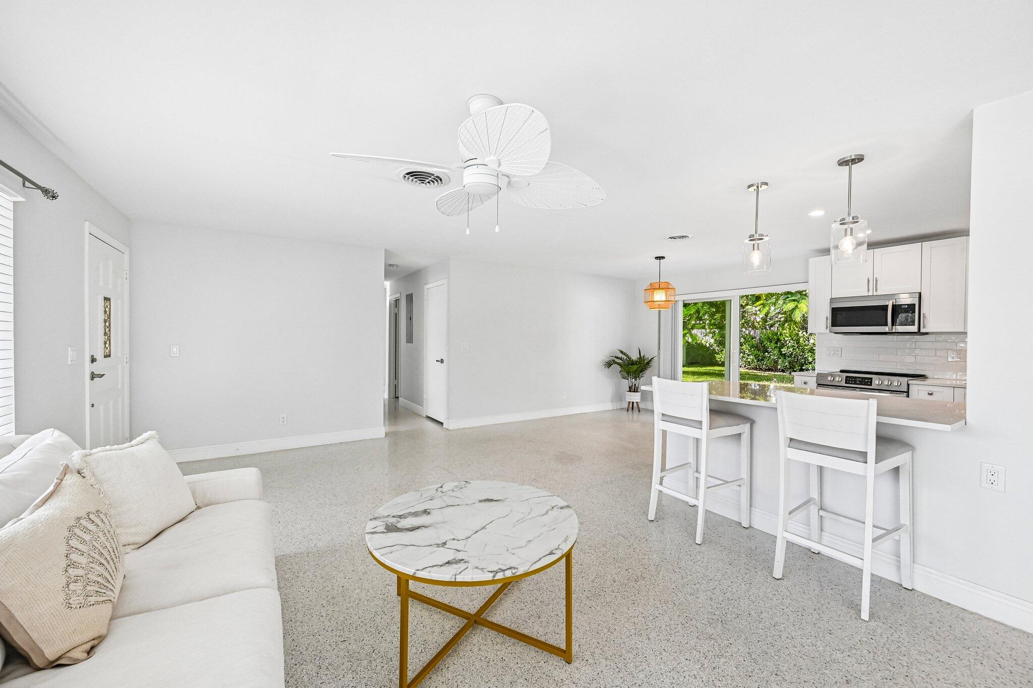 Bright living room opens to a white kitchen, with a marble coffee table and breakfast bar.