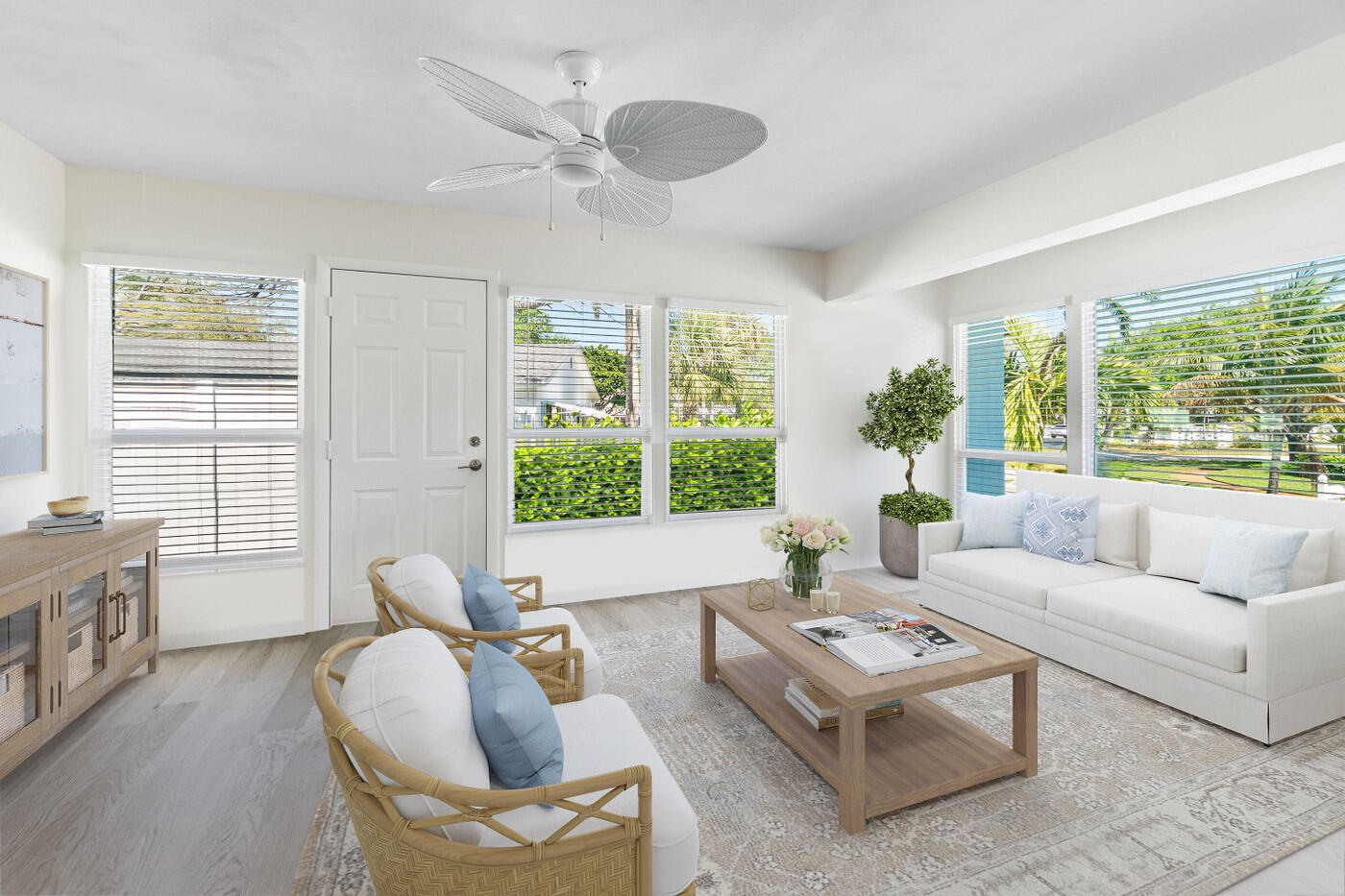 Bright living room with a white sofa, wicker chairs, and wide windows overlooking palms.