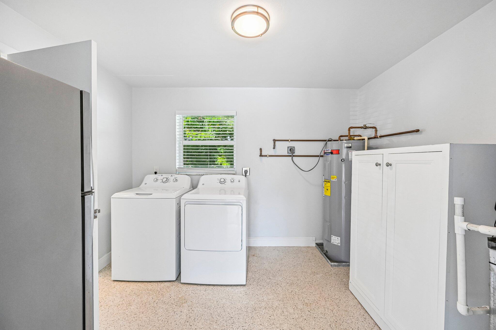 Laundry room with a washer, dryer, water heater, and storage cabinets.