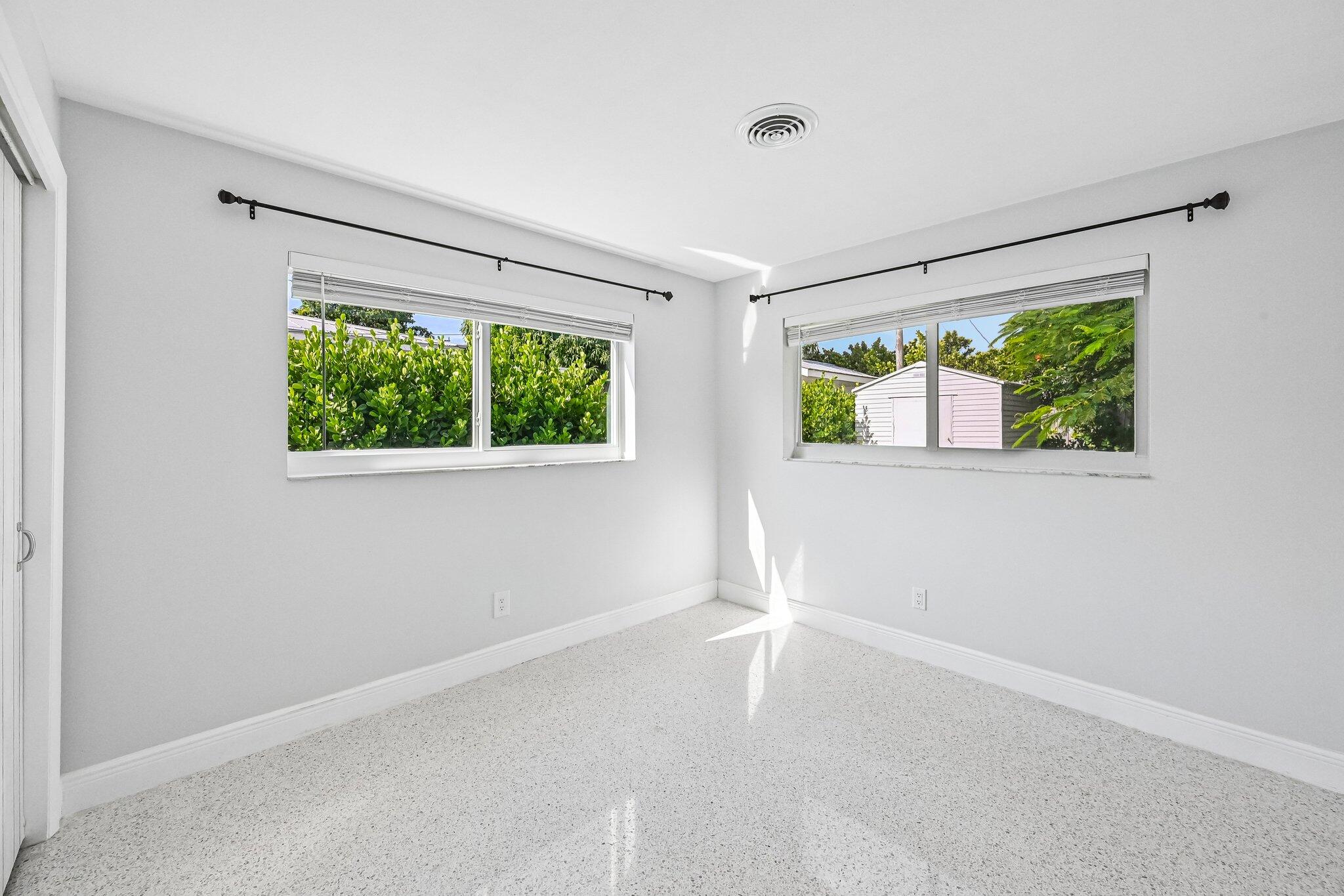 Empty bedroom with two windows, white blinds, and light-speckled flooring.