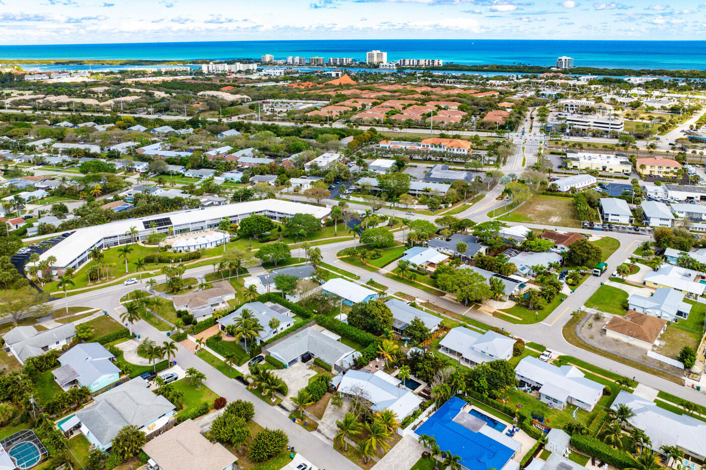Aerial view of a coastal neighborhood with homes, swimming pools, and ocean in the distance.