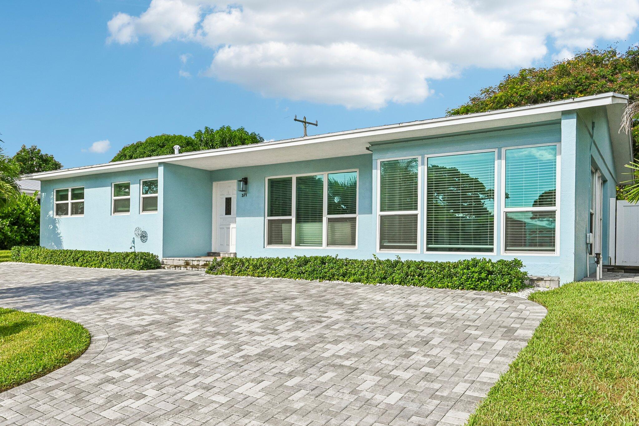 Light blue single-story home with a broad paver driveway and large front windows.