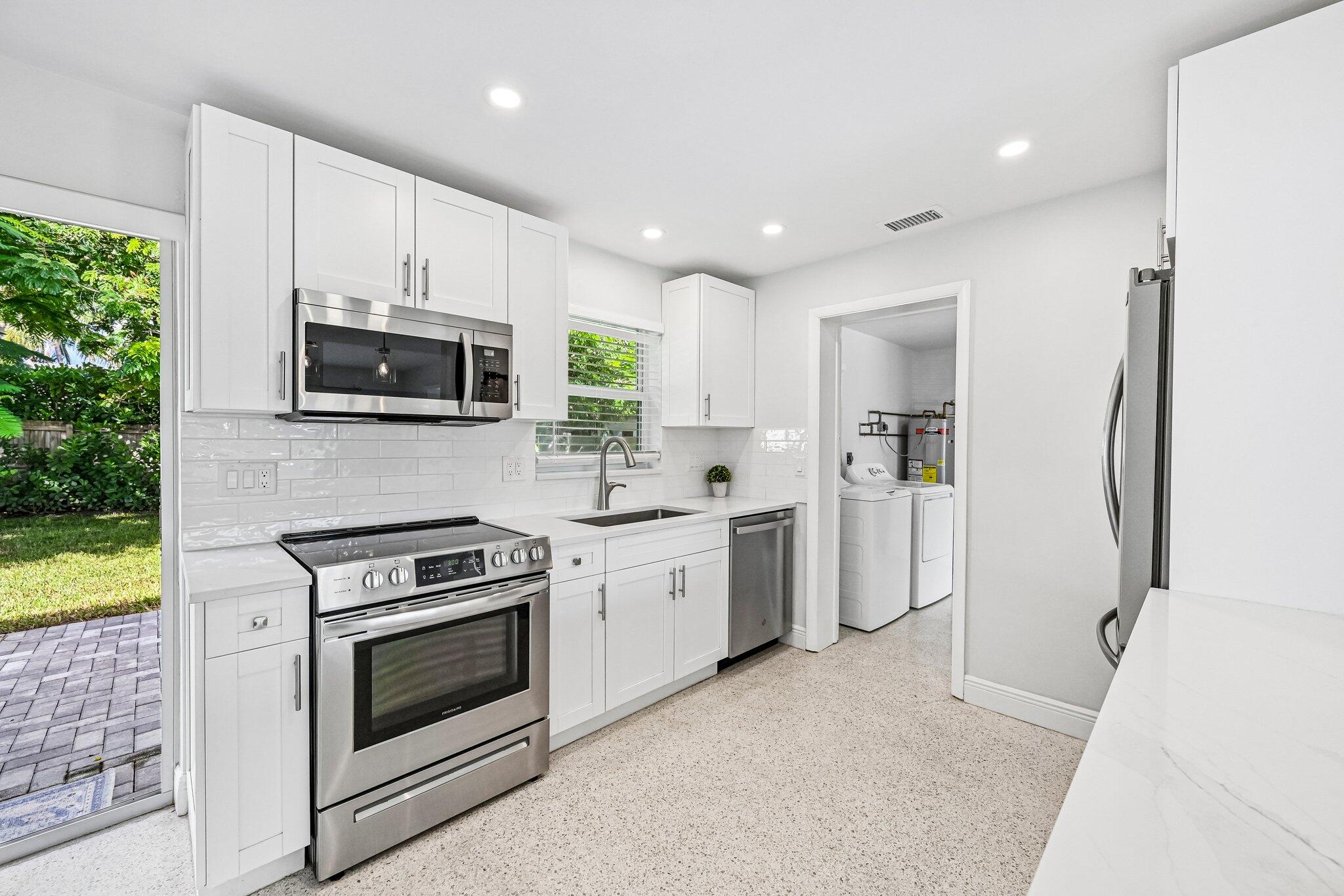 Bright white kitchen with stainless appliances, subway tile backsplash, and doorway to laundry area.